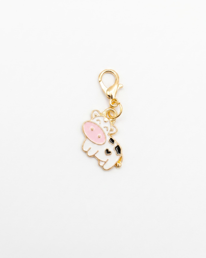 Golden and enamel charm with lobster hook showing a white cow with black spots