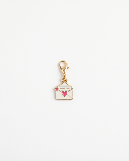 Golden and enamel charm with lobster hook showing a letter with a heart on the opening
