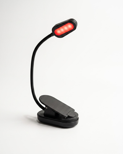 Black clip-on rechargeable reading light with adjustable flexible neck and red LED illumination angled downward for reading in bed.