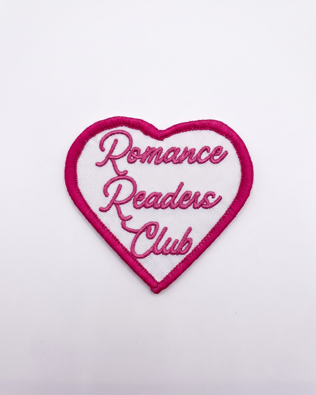 a white heart shape patch with pink boards, in the heart the text says 'Romance Readers Club'